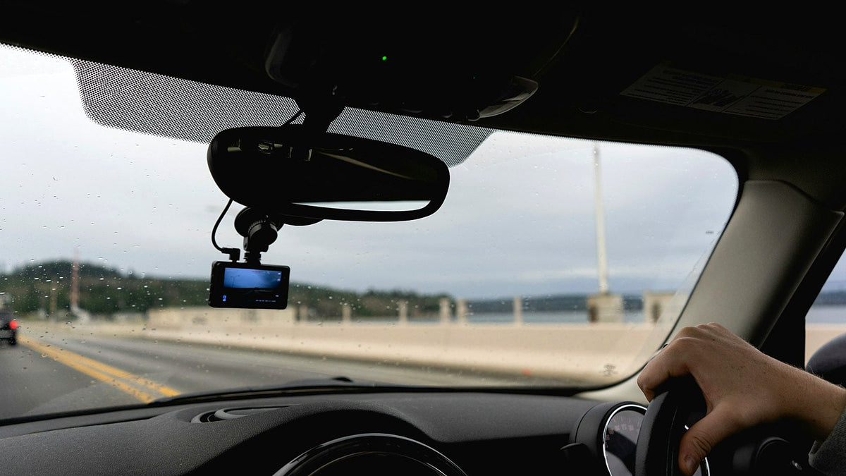 A dash cam mounted under the rear-view mirror of a car, with the road ahead through the windscreen