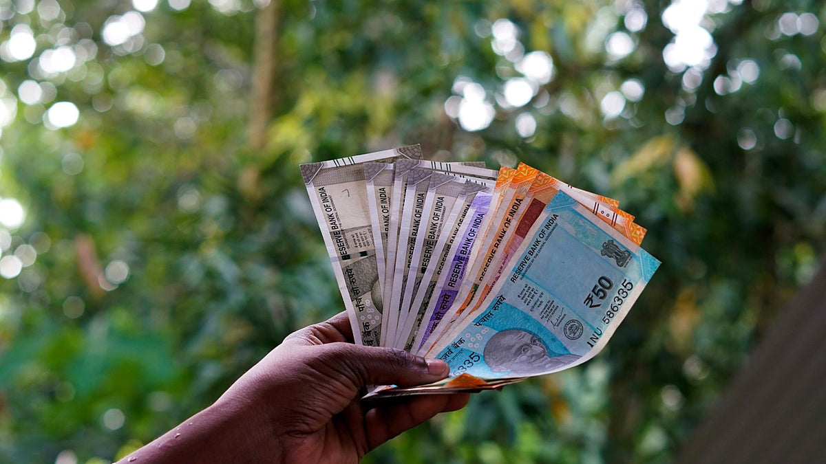A hand holding a fan of Indian rupee notes outdoors