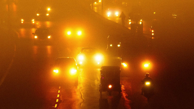 Headlights of cars and an auto-rickshaw glaring through fog on an Indian road at night