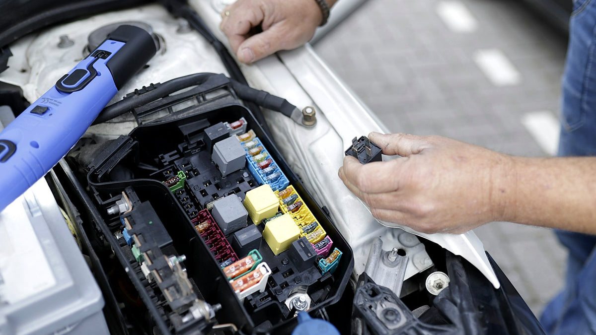 A mechanic's hand holding a relay beside a car's open fuse box