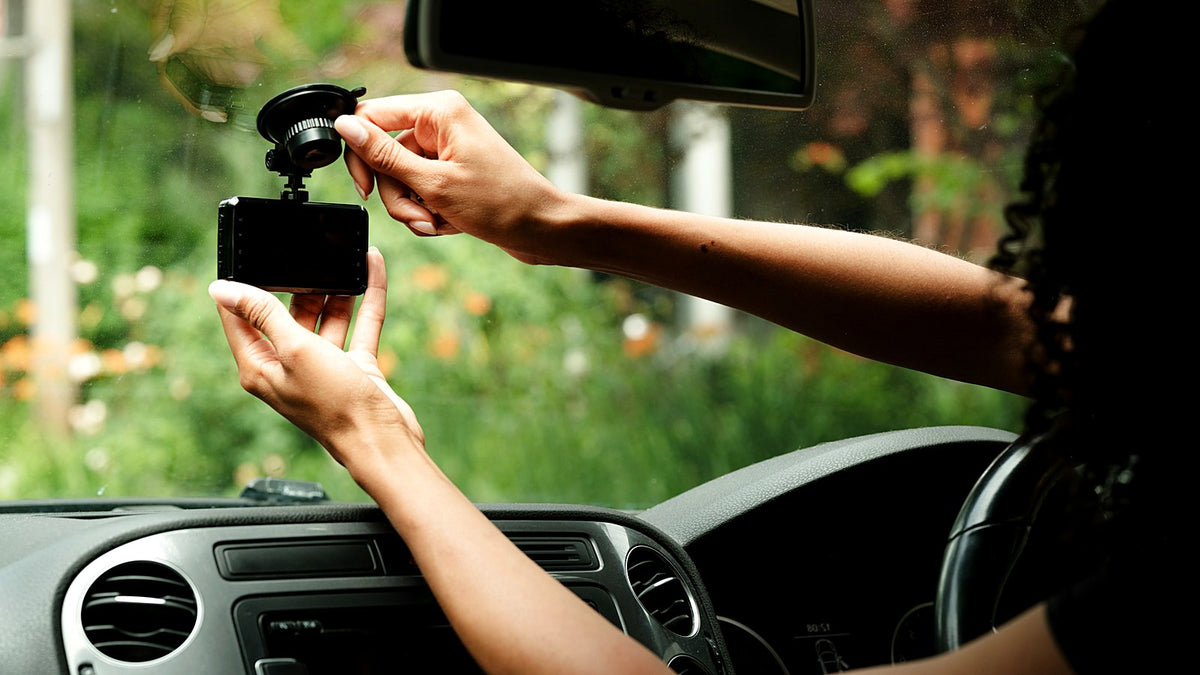 Hands fixing a dash cam to a car windscreen with a suction mount