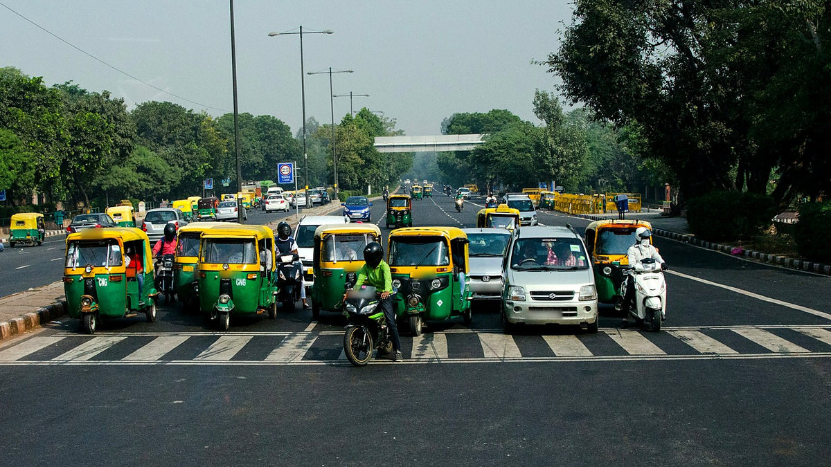 Auto-rickshaws, cars and bikes waiting at a stop line on a Delhi road