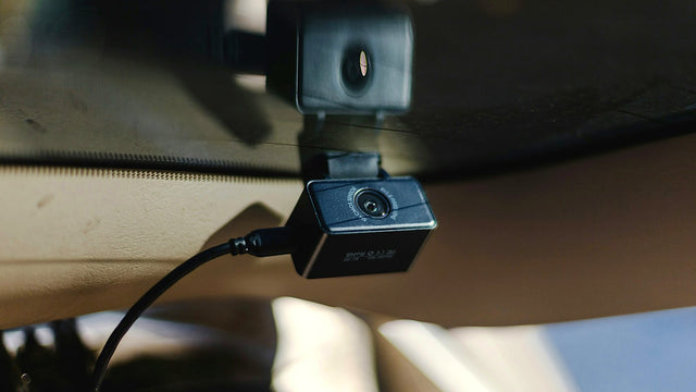 Close-up of a small dash cam and its power cable fixed to a car windscreen